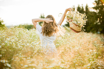 Happy girl on the camomile field, summer sunset. in a white dress. running and spinning, the wind...
