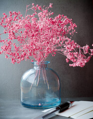 Still life. Small pink flowers in a glass bottle, pen and blank forms. Gray background. Selective focus - 365012310