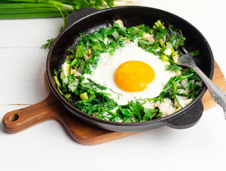 Green shakshuka. Fried eggs with fresh arugula, green onions, dill in a pan