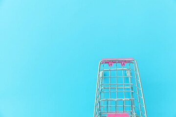 Small supermarket grocery push cart for shopping toy with wheels isolated on blue pastel colorful trendy background Copy space. Sale buy mall market shop consumer concept.