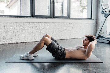 side view of shirtless sportsman doing sit ups on fitness mat in gym