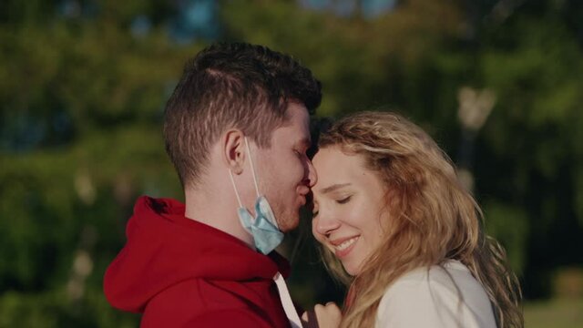 Pretty couple meet after long self isolation. Young man and woman take off medical mask and kiss. Pandemic is over. Finally end of quarantine. Health care and medical concept. Happy people.