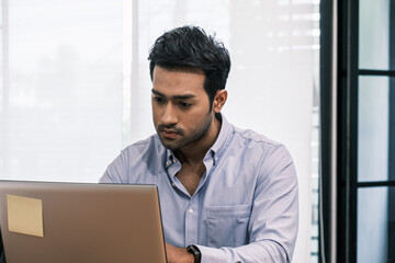 Fototapeta premium An Asian teenage man is sitting on a desk with a notebook. He is a company manager. he works hard to make the company successful.
