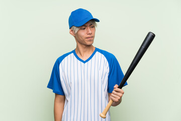 Young asian man playing baseball over isolated green background with sad expression