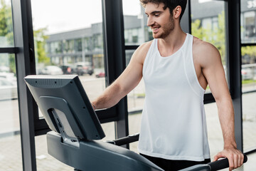 Fototapeta na wymiar happy sportsman looking at screen on modern treadmill in gym