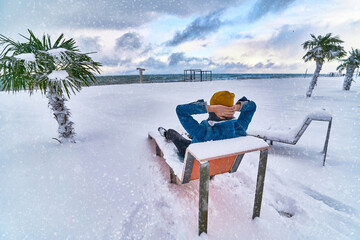 Traveler resting on a deck chair among evergreen tropical palm trees covered white snow standing in...