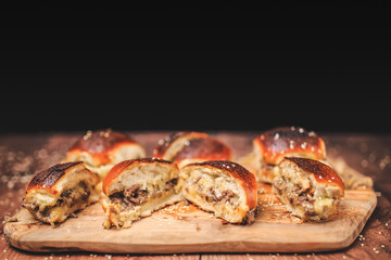 Homemade beef burger with cheese sliced in half with other burgers on the side on a wooden board with free space for text/decoration. Interior view of the burger.