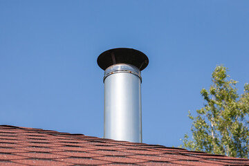 Stainless steel metal chimney pipe on the roof of the house against the sky.