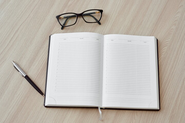 Fototapeta premium Open blank daily planner, pen, glasses on light wooden background. Top view