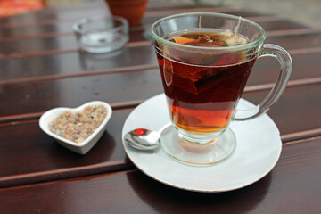 Close up of a glass cup of black tea including swimming tea bag on wooden table outside