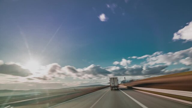A drive on the highway in Czechia. Cars and trucks passing. White clouds hanging on the sky. Green farm fields stretch on both sides of the road. A hyperlapse video.