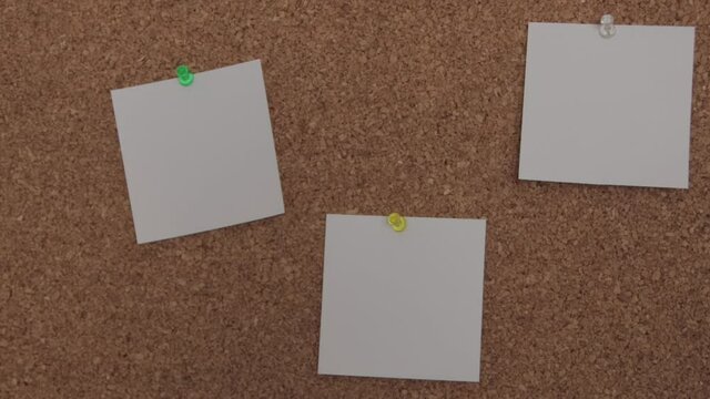 A young white woman pins a third white paper to the notes on a corkboard