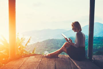 Female is typing something in diary on touch pad, while is sitting against amazing Asian landscape...
