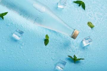 Cold Water Bottle, ice cubes, drops and mint leaves on a blue background.