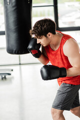 athletic man in sportswear and boxing gloves working out with punching bag