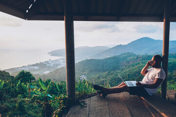 Hipster gut traveler working remote while enjoying Thailand nature landscape during summer...