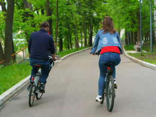 Photography of couple of young man and woman biking in the public park in Moscow. Healthy urban lifestyles. Backs / rear view.
