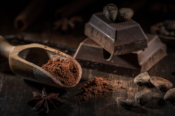 Wooden scoop with cocoa powder and piece of block chocolate with cacao beans. 