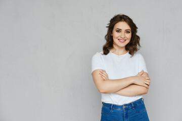 Positive girl in jeans, t-shirt and stilettos posing near the wall
