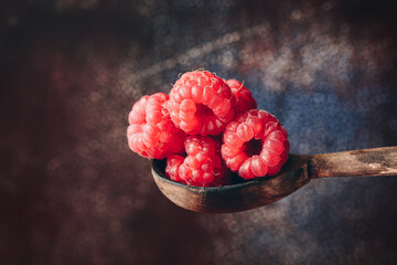 Closeup fresh raspberries in a wooden spoon on a dark rustic backdrop. Selective focus. Rustic...
