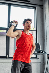 sportive man working out with dumbbell while standing with hand on hip