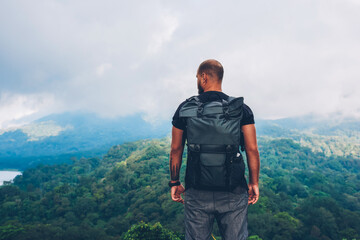 Fototapeta na wymiar Back view of young man lover of travel standing on top of mountain and admiring amazing scenery of rainforest and green landscapes in asia environment while enjoying adventure lifestyle in treks