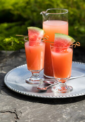 Guava juice with watermelon wedges served on a metal tray outdoors.