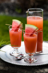 Guava juice garnished with watermelon wedges, outdoors and ready for drinking.