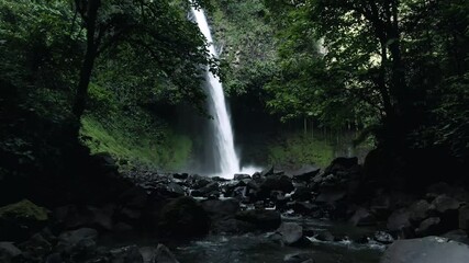 Aerial flight between trees revealing majestic La Fortuna volcanic waterfall