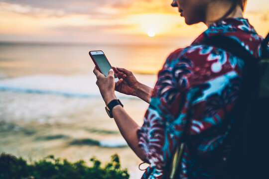 Cropped image of woman traveler dressed in stylish shirt communicating with friends via roaming internet in smartphone outdoors.Hipster girl using modern technology while standing near to ocean