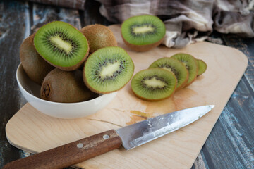 cut and whole kiwi on a cutting Board and in a dish, wooden background