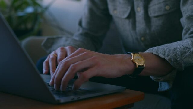 Fashionable caucasian home worker with focused eyes through his glasses, handheld camera tilting down to his hands moving on the laptop, Concept of independent businessman starting business from home