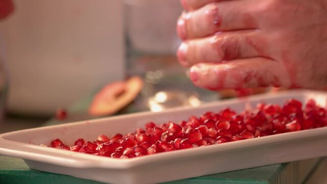 Male hands peeling pomegranate at kitchen close up. Plate with red ripe pomegranate seeds on table.