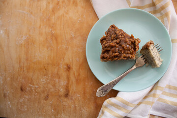 piece of pie covered with caramel and sunflower seeds in light blue plate with fork on the left side of a wooden background
