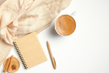 Cozy home desk with female beige scarf, cup of coffee, paper notebook, cinnamon sticks. Autumn or winter concept. Flat lay, top view.