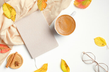 Autumn, fall concept. Flat lay composition with paper notebook, cup of coffee, fashion glasses, fallen leaves, beige scarf on white background. Hygge style feminine workspace.