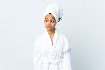 Young woman in bathrobe over isolated white background making doubts gesture looking side