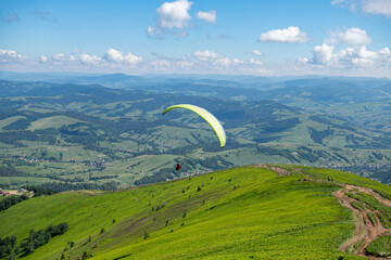 Paragliding in the Carpathians in the summer.Two paragliders fly over a mountain valley on a sunny summer day. Beautiful landscape with greenery and people paragliding. Rest and travel.