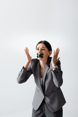 emotional businesswoman with scotch tape on mouth gesturing isolated on white