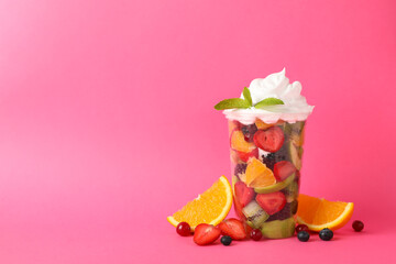 Fruit salad in takeaway cup on pink background, space for text