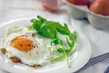 Fried eggs and rucola leaves on a white plate