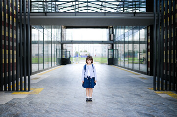 happy girl schoolgirl 8 years of European appearance with a backpack sitting goes in school uniform in the school yard looking at the camera closeup