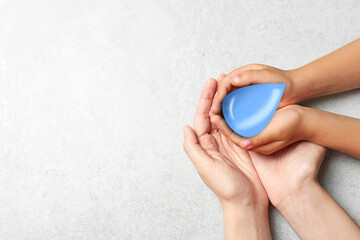 Woman and her child holding water drop on grey stone background, top view with space for text. Ecology protection