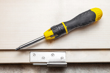 Screwdriver and door hinges on a wooden door