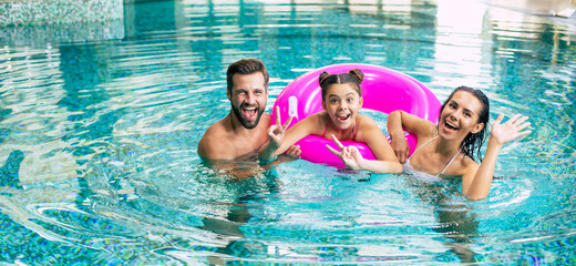 Excited and young happy family on vacation in the spa hotel are relaxing and have fun in the swimming pool. Summer rest