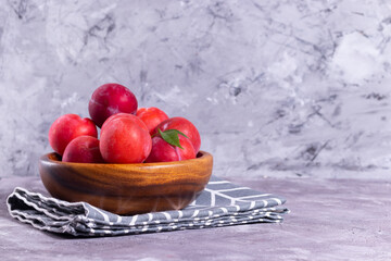 Ripe plums in a wooden plate with a tissue napkin on a gray background