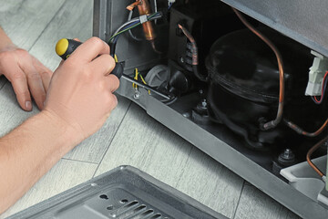 Repairman with screwdriver fixing refrigerator indoors, closeup
