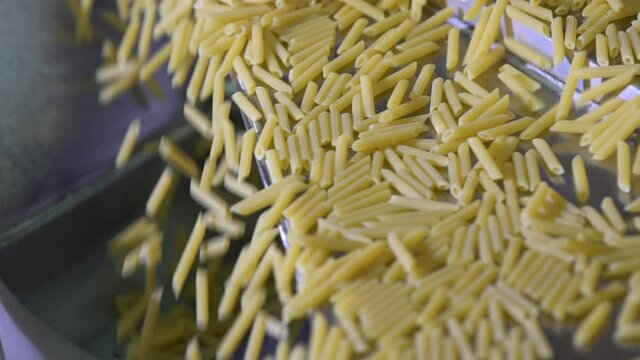 Close up slow motion of raw dried organic penne macaroni running on a steel conveyor belt in an Italian pasta factory. Healthy food.