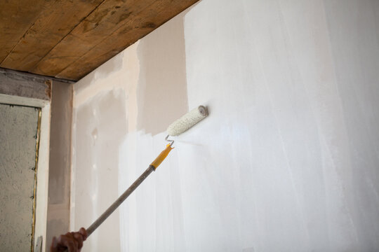 White paint roller in hand with drywall wall.