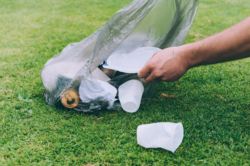 Guy picks up trash from nature in a waste bag.